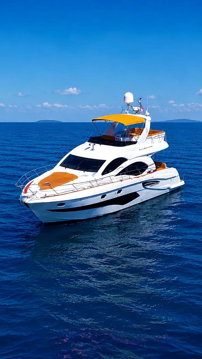White and orange luxury yacht anchored in clear blue Mediterranean waters with islands visible on horizon