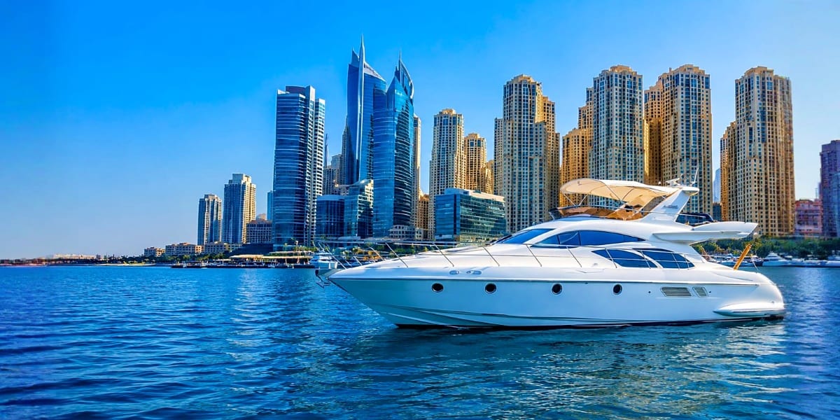 Luxury white and blue yacht anchored in turquoise water with Dubai Marina skyscraper skyline in background under clear blue s