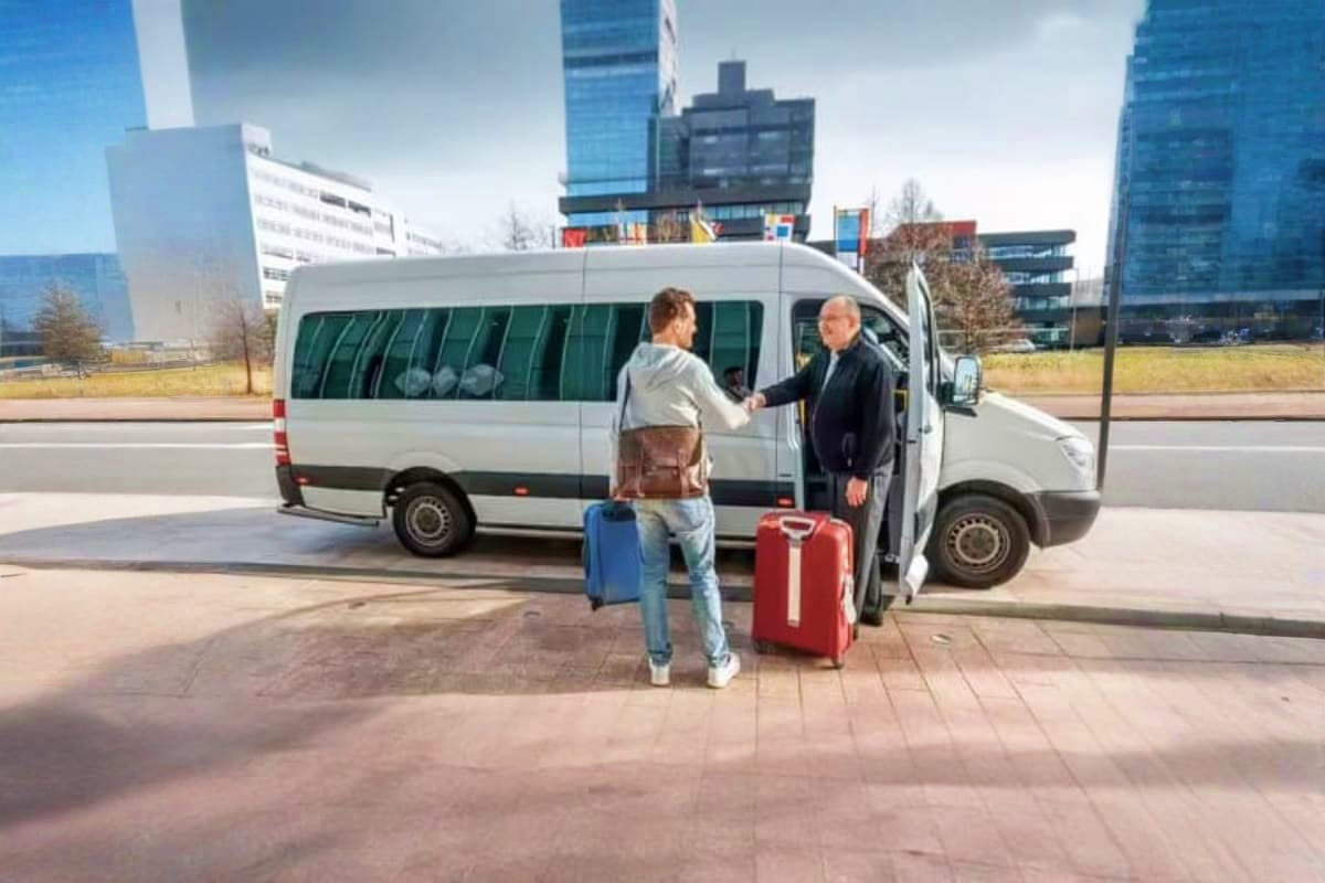 Driver greeting passenger with luggage at white van for airport transfer service in modern city setting