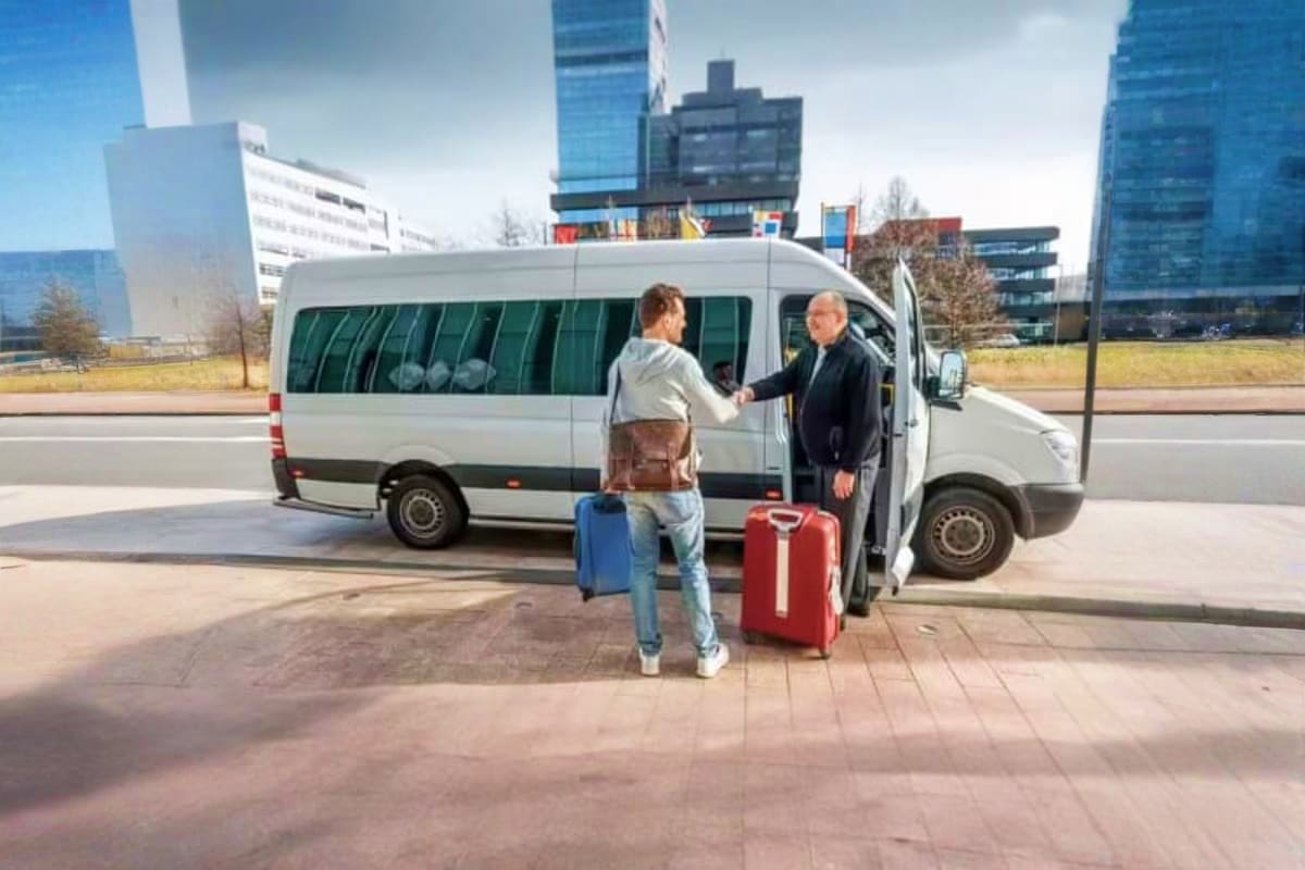 Passenger with luggage boarding white shuttle van at modern airport with city skyscrapers in background