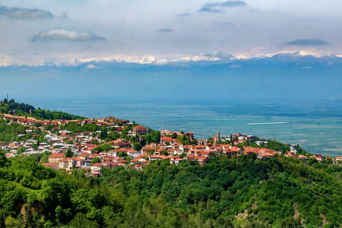 Sighnaghi town perched on hillside overlooking Alazani Valley with snow-capped Caucasus Mountains in background, Georgia