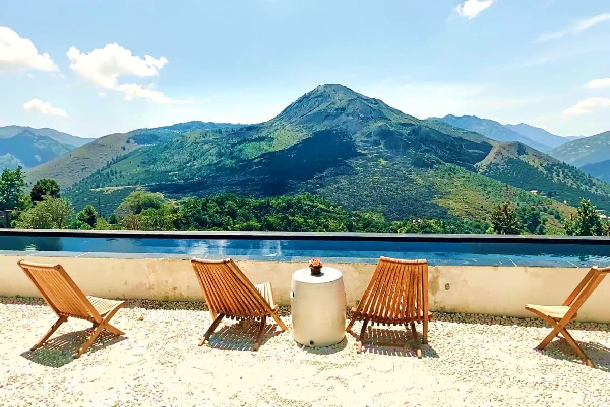Wooden lounge chairs facing infinity pool overlooking Mount Batur volcano and green forested hills in Bali
