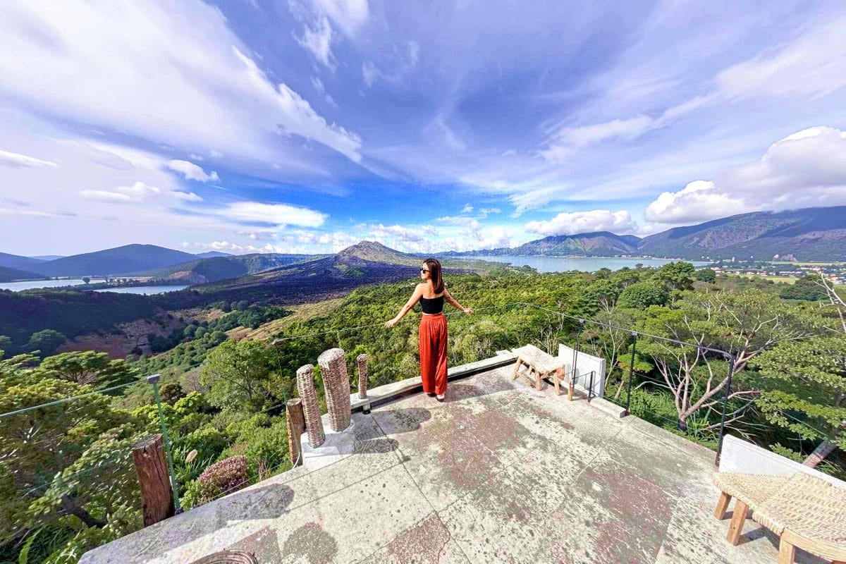 Woman standing on viewing platform overlooking Kintamani volcanic landscape with mountains, lakes and lush green forests