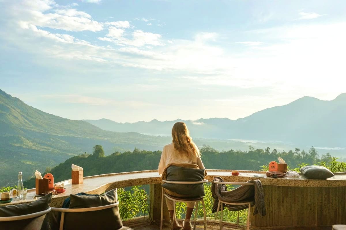 Woman sitting on terrace overlooking Kintamani volcanic mountains and lake valley in Bali