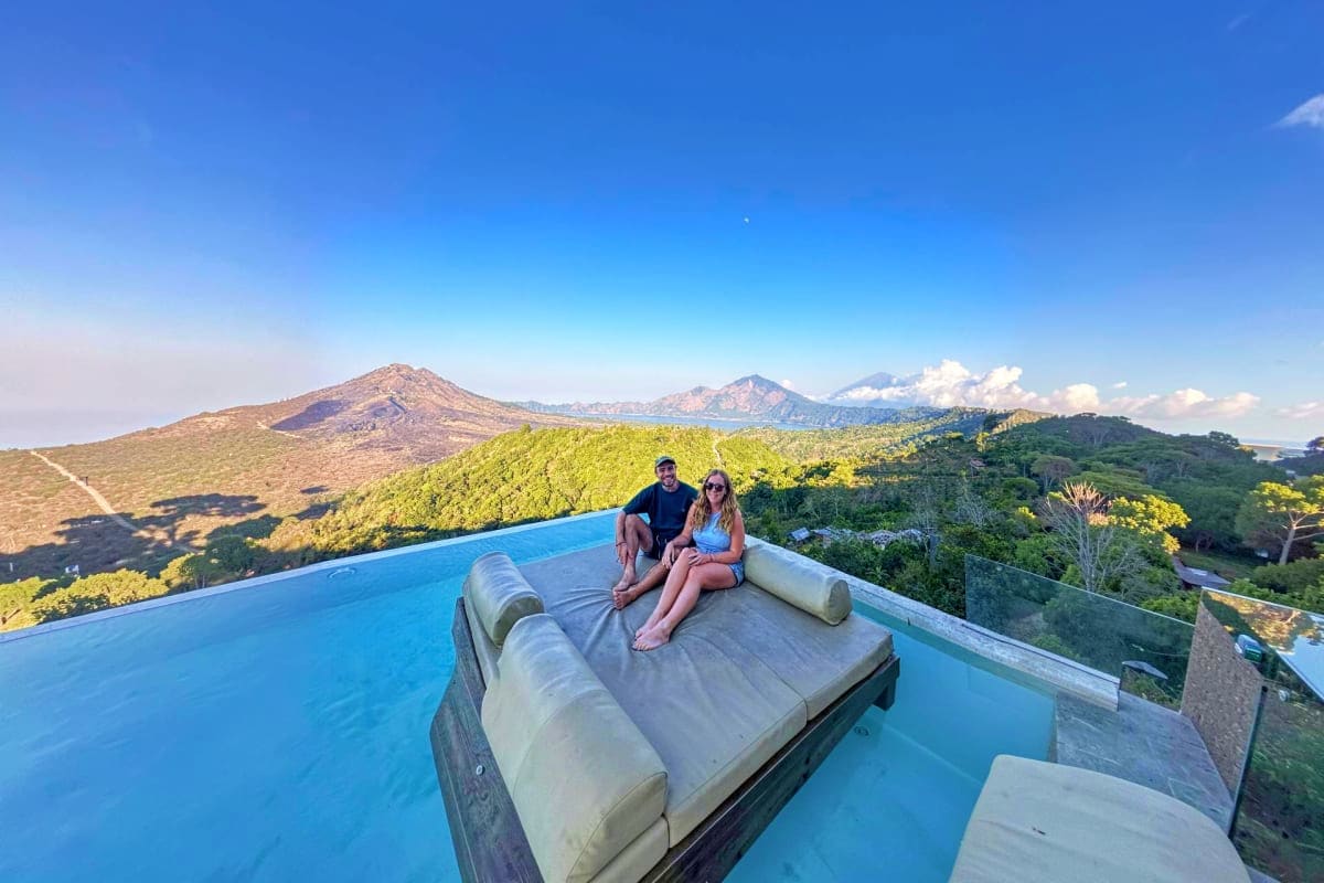 Couple relaxing on lounge bed at infinity pool overlooking Kintamani volcanic mountains and lush green valleys in Bali