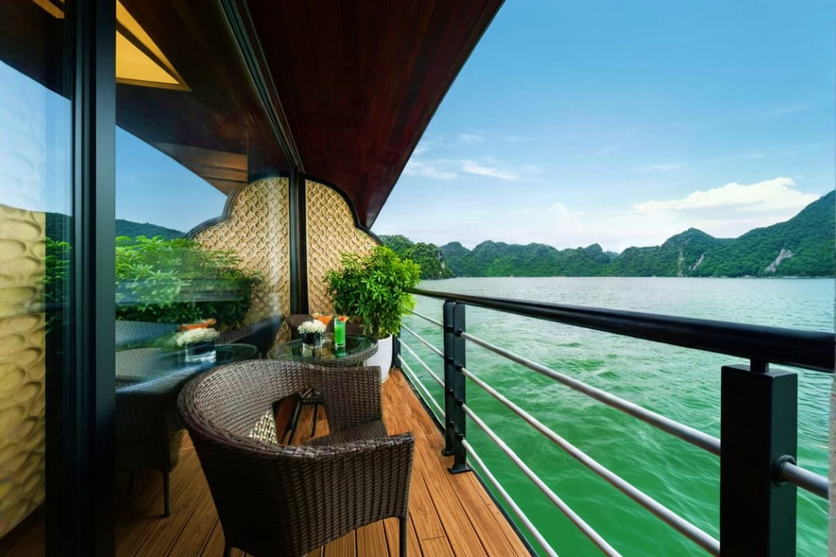 Modern waterfront terrace with wicker seating overlooking Ha Long Bay's emerald waters and limestone mountains under clear sk
