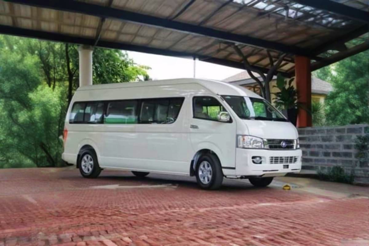 White passenger van parked under covered carport with brick driveway and green landscaping