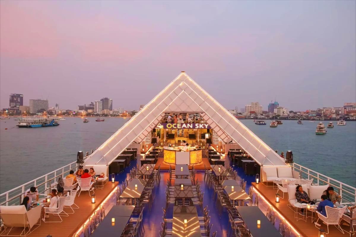 Illuminated rooftop deck of Ocean Sky dinner cruise ship at dusk with passengers dining, city skyline and harbor visible in b