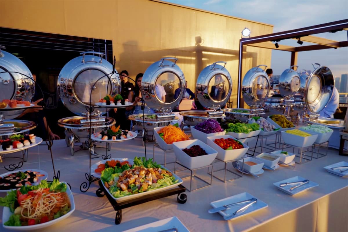 Rooftop dinner buffet setup with spherical dining pods, fresh salads, and colorful vegetables under golden sunset lighting, P