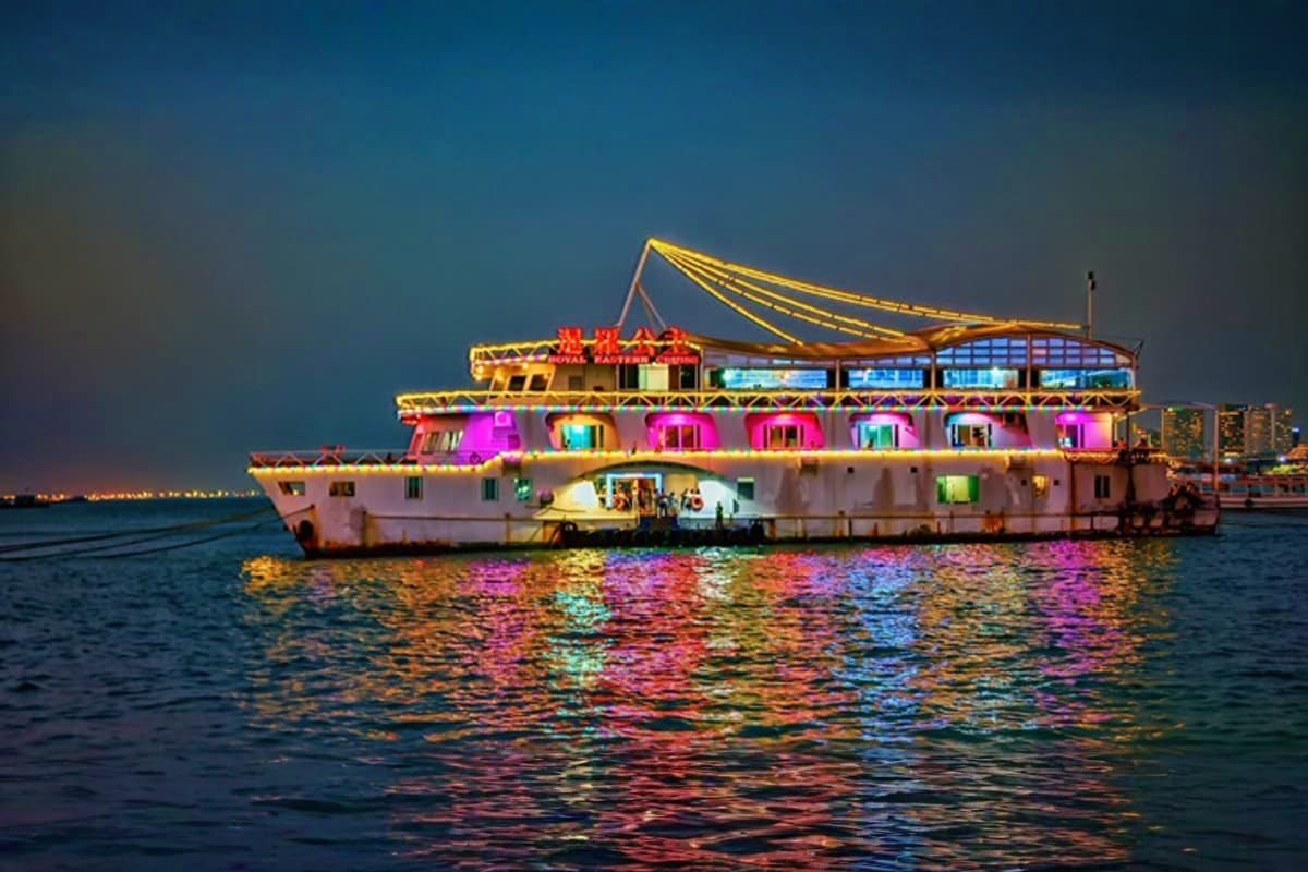 Illuminated multi-deck cruise ship Atlantis at night in Pattaya waters with colorful LED lighting reflecting on the sea