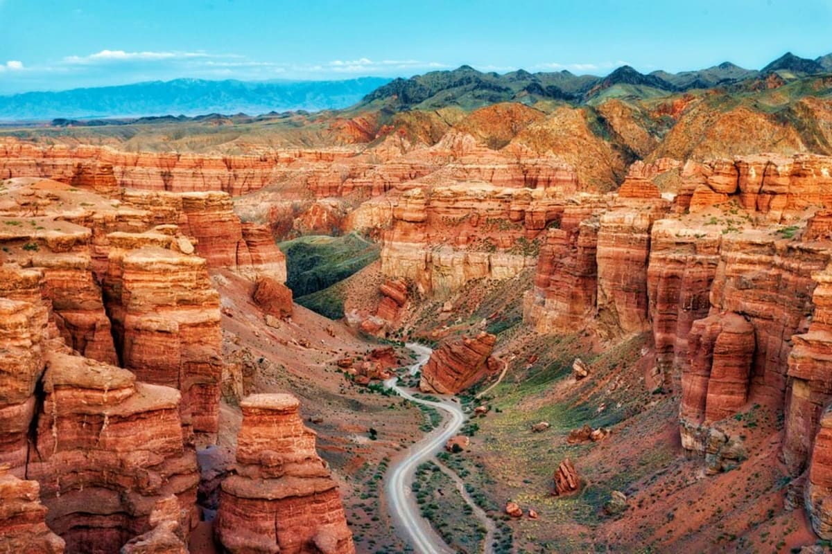 Full Day Charyn Canyon, Lunar Canyon, Black Canyon Tour with Charyn River Aerial view of winding road through red rock canyon formations with river, mountains in distance under blue sky