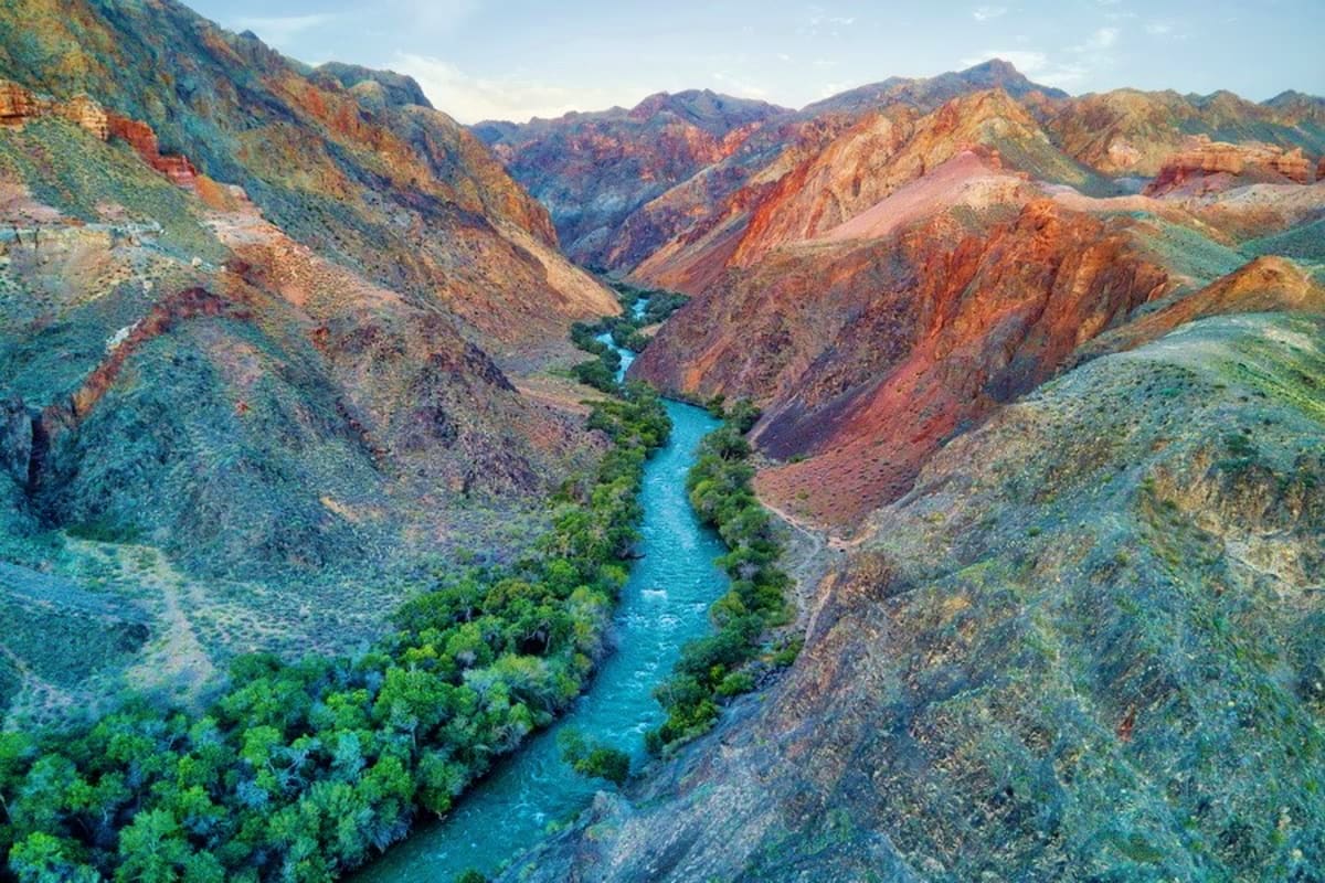 Full Day Charyn Canyon, Lunar Canyon, Black Canyon Tour with Charyn River Turquoise river flowing through a deep canyon with colorful layered rock formations and green vegetation lining the banks