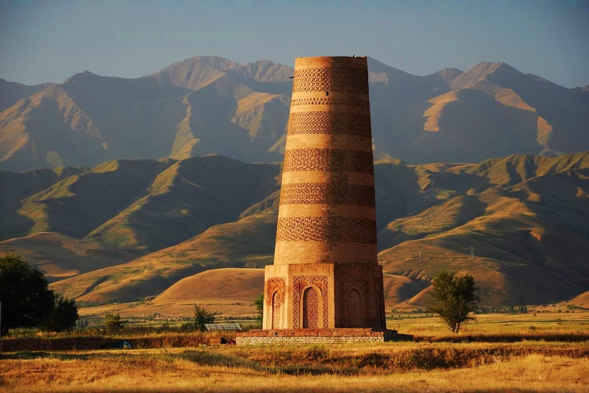 Ancient brick Burana Tower with intricate geometric patterns standing in golden grassland with snow-capped mountains in backg