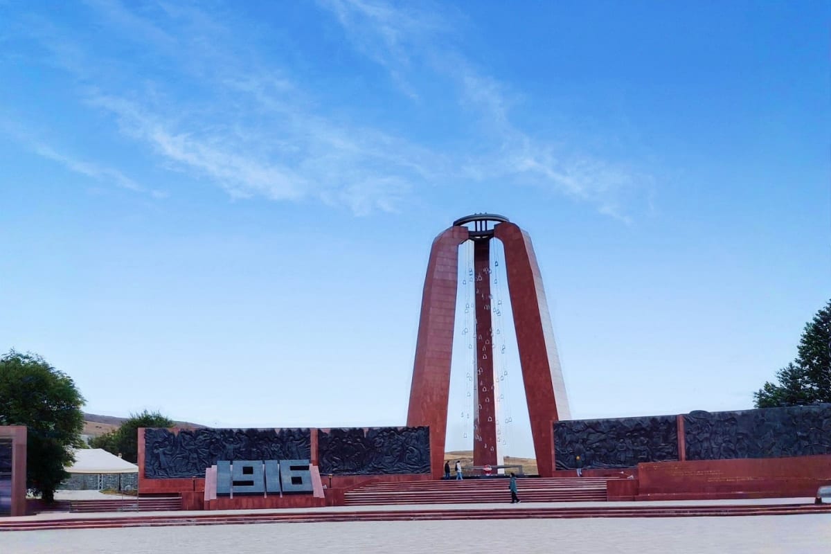 Large red and white memorial monument with architectural structures and relief panels under blue sky at Ata Beyit historical 