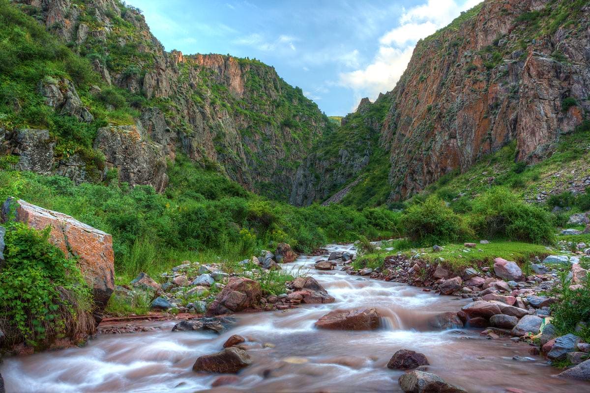 Mountain river flowing through rocky canyon with steep cliff walls and lush green vegetation under blue sky