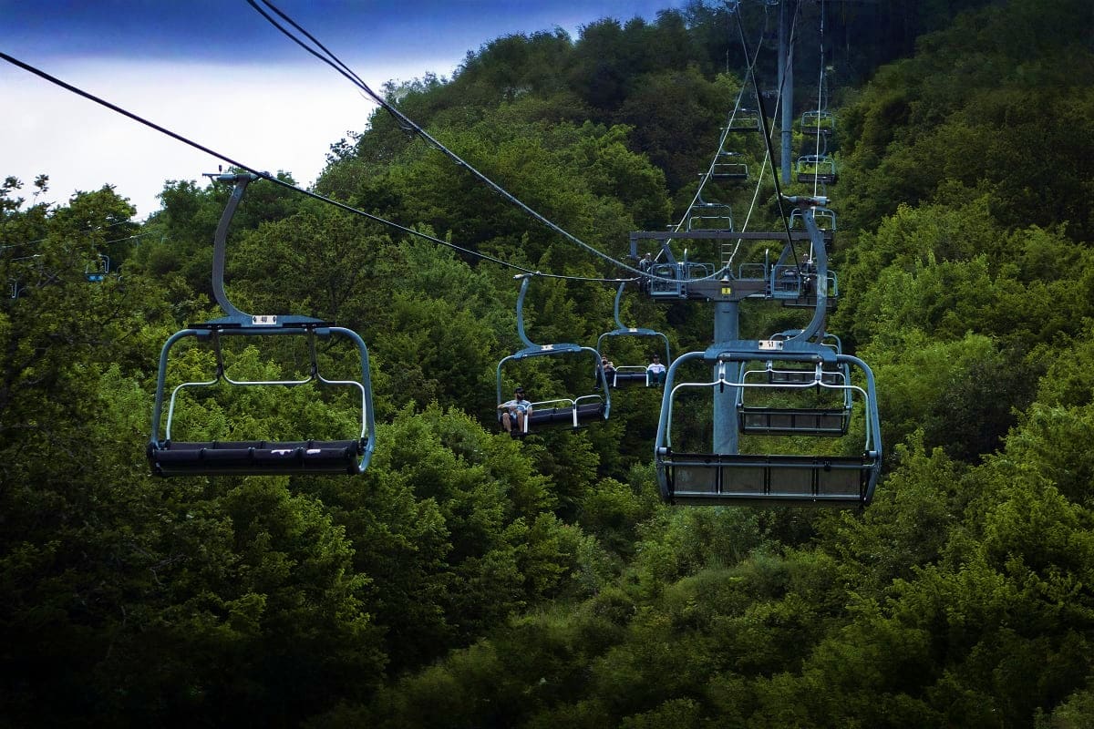 Ski lift chairs suspended over forested mountains, transporting visitors above dense green trees in Tsaghkadzor ski resort ar