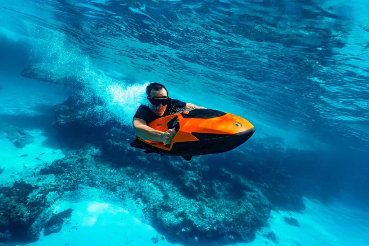 Sea Bob Dubai 30min Man riding orange and black Sea Bob underwater scooter above coral reef in clear blue ocean water