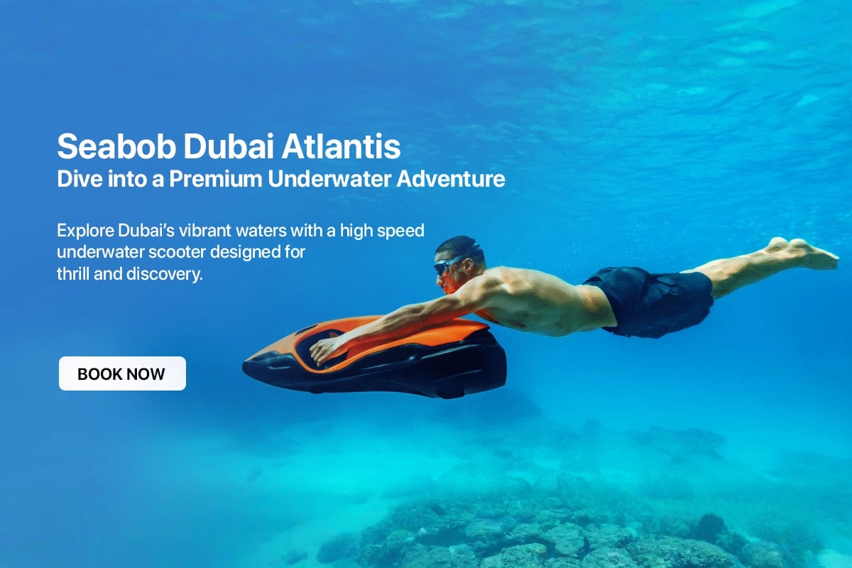 Man riding orange and black underwater scooter in clear blue Dubai waters with coral reef below