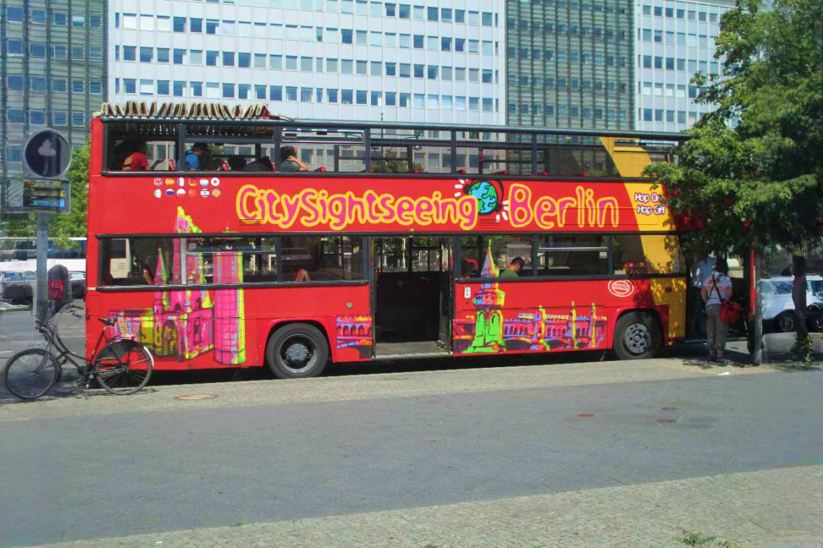 Red double-decker Hop-On Hop-Off tour bus with "City Sightseeing Berlin" branding parked on urban street with office building
