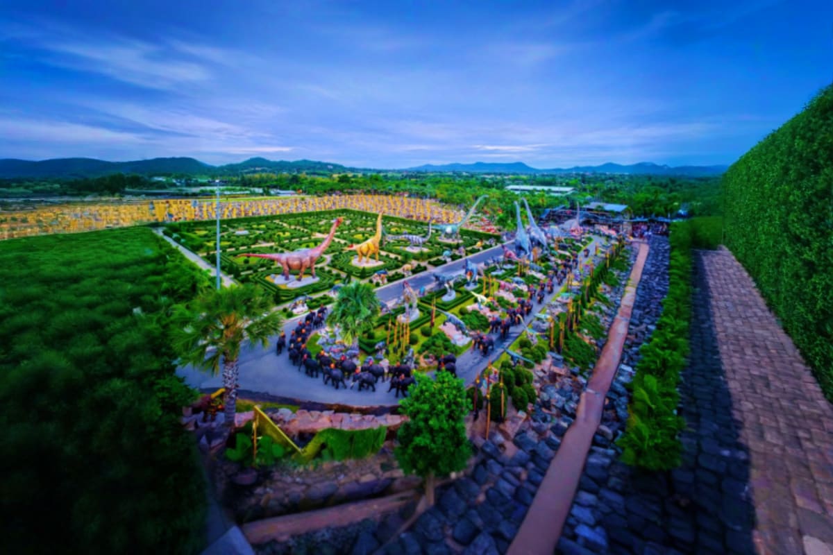 Aerial view of Nong Nooch Tropical Garden with dinosaur sculptures, landscaped pathways, water features, and green mountains 