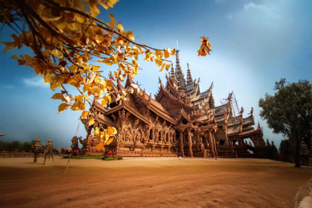 Traditional Thai wooden temple with ornate spires and golden autumn foliage framing the entrance courtyard at Sanctuary of Tr