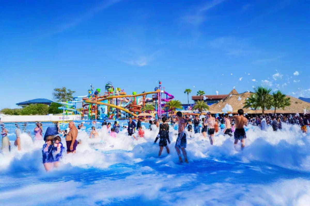 Crowded wave pool at Columbia Pictures Aquaverse Waterpark with colorful water slides and attractions in background under blu