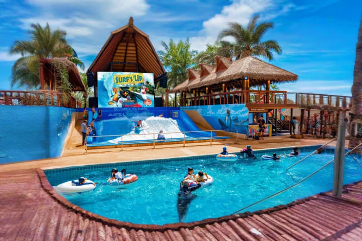 Surf's Up wave pool at Columbia Pictures Aquaverse with visitors on floats, artificial wave machine, thatched-roof structures