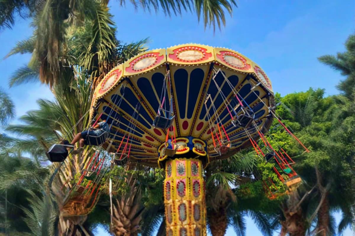 Colorful chairlift carousel ride with red and gold decorative canopy at Pattaya Park amusement park surrounded by palm trees