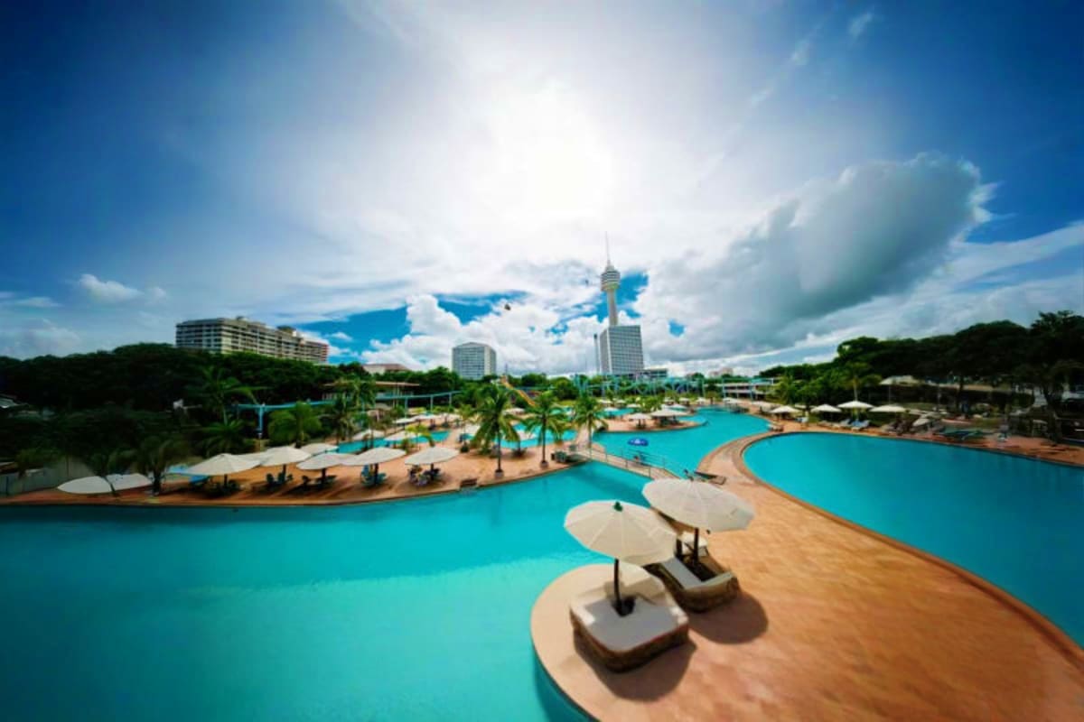 Aerial view of Pattaya Park with turquoise pools, sandy beaches, palm trees, lounge chairs, and high-rise hotels under blue s