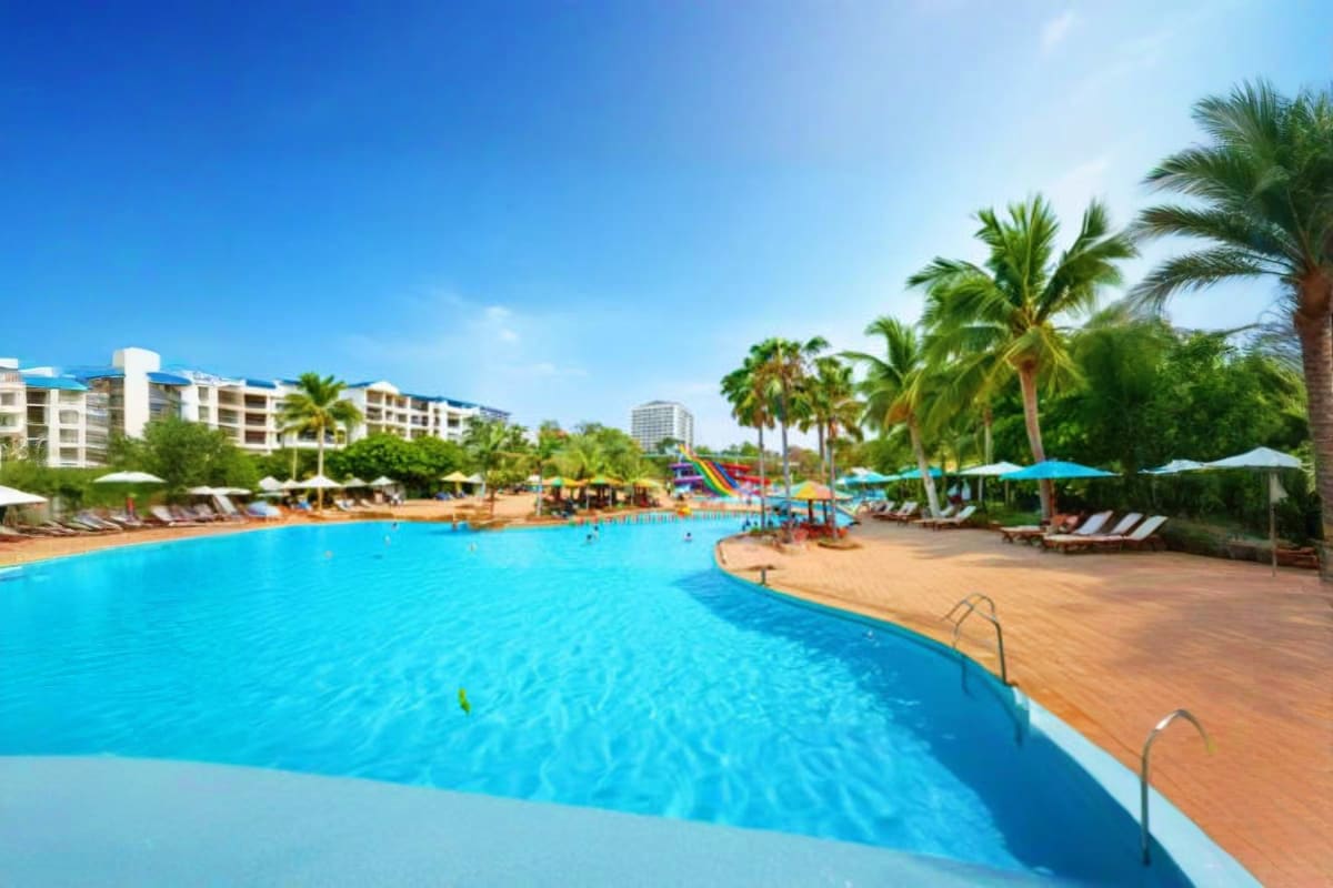 Large resort pool with crystal blue water, palm trees, loungers, umbrellas, and white apartment buildings in background at Pa