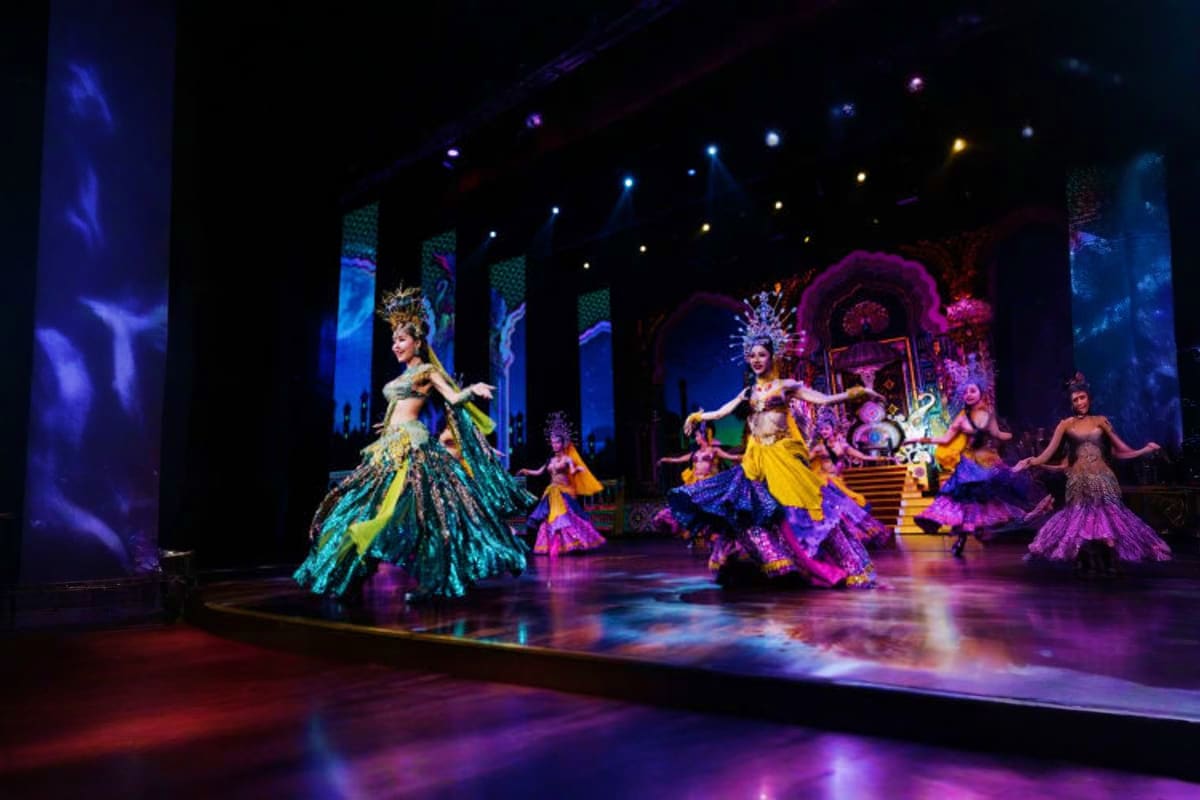 Alcazar Show theatrical performance with dancers in elaborate colorful costumes on illuminated stage with blue and purple lig