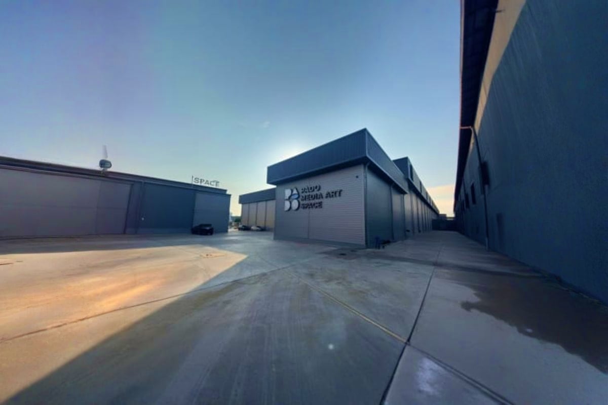 Modern industrial warehouse buildings with signage for Padomedia Art Space in an empty lot under clear sky