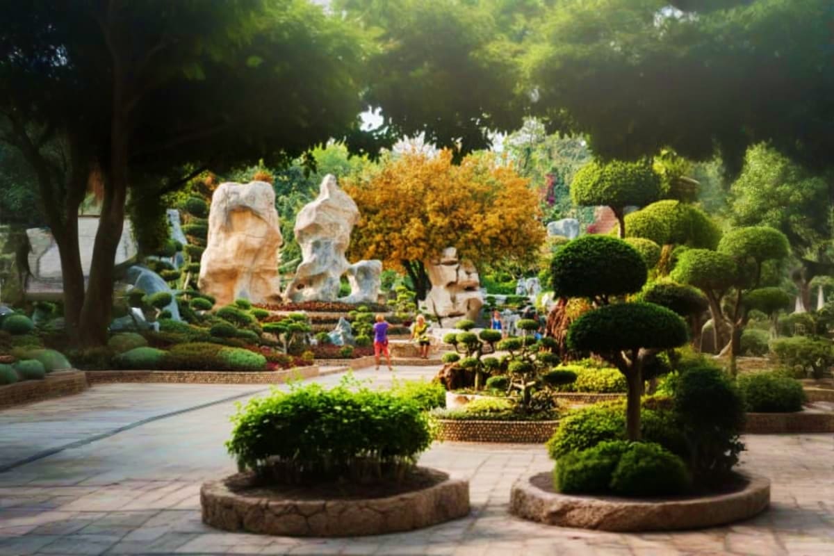 Scenic garden pathway with stone sculptures, manicured topiary plants, flowering shrubs, and visitors at Million Years Stone 