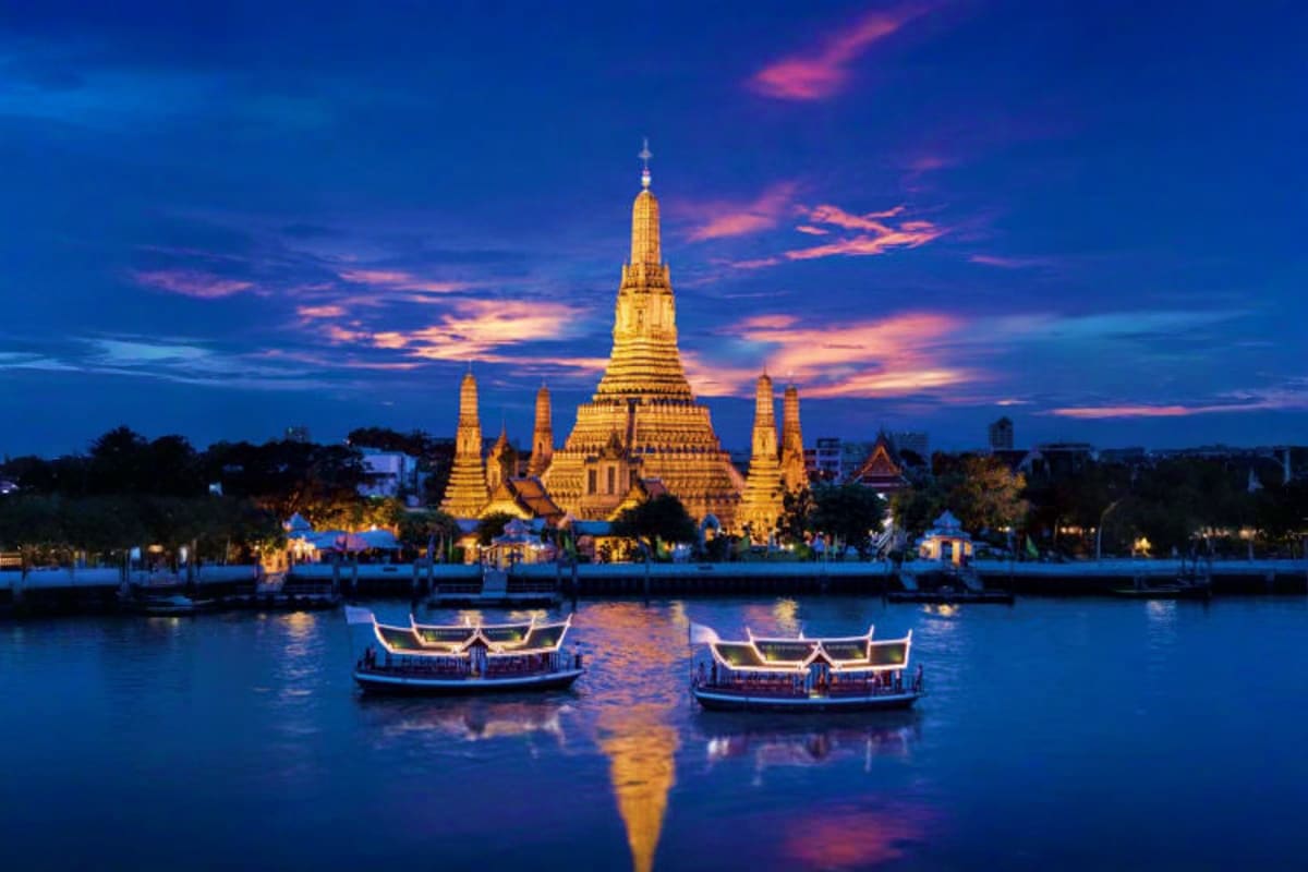Chaophraya Dinner Cruise Wat Arun illuminated at dusk with traditional long-tail boats on the Chao Phraya River in Bangkok