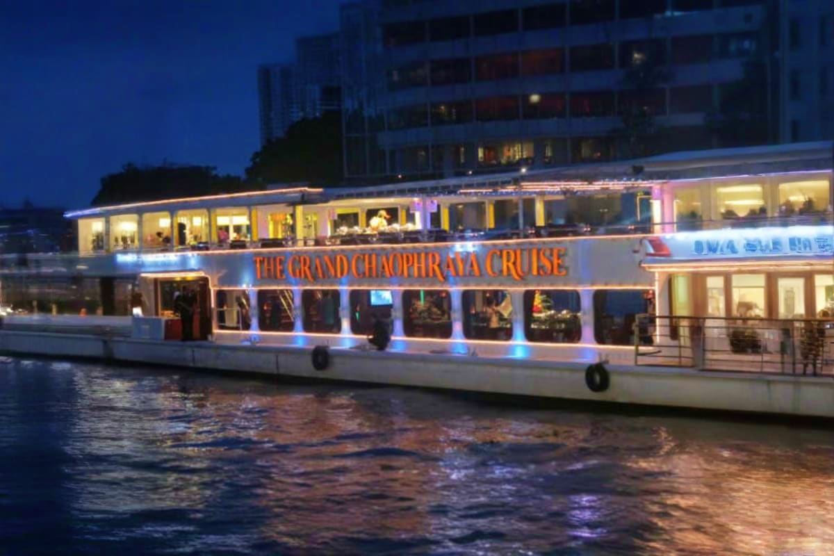 Illuminated Grand Chaophraya Cruise boat on the river at dusk with lit windows and passengers visible inside