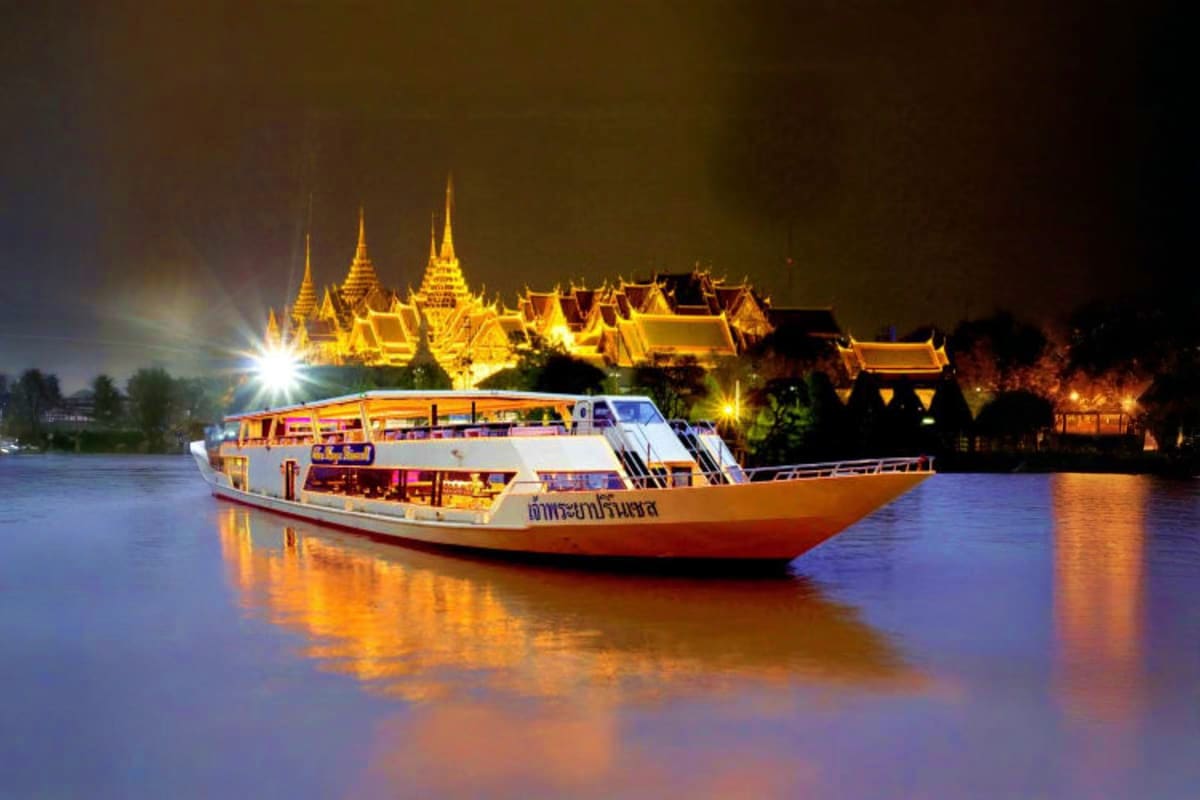 Illuminated dinner cruise boat on the Chao Phraya River with golden-lit Thai temple in the background at night