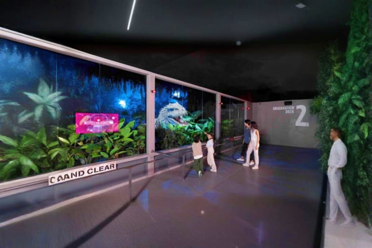 Jurassic World Park Modern museum exhibition space with visitors viewing dinosaur displays behind glass, tropical plants, neon signage, and "Obse