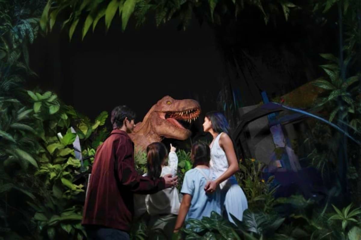 Jurassic World Park Family of visitors encountering a realistic dinosaur animatronic in a jungle-themed attraction with tropical plants and dark