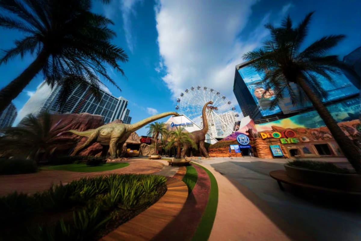 Jurassic World Park Dinosaur sculptures and themed attractions at Jurassic World Park with Ferris wheel and palm trees under blue sky