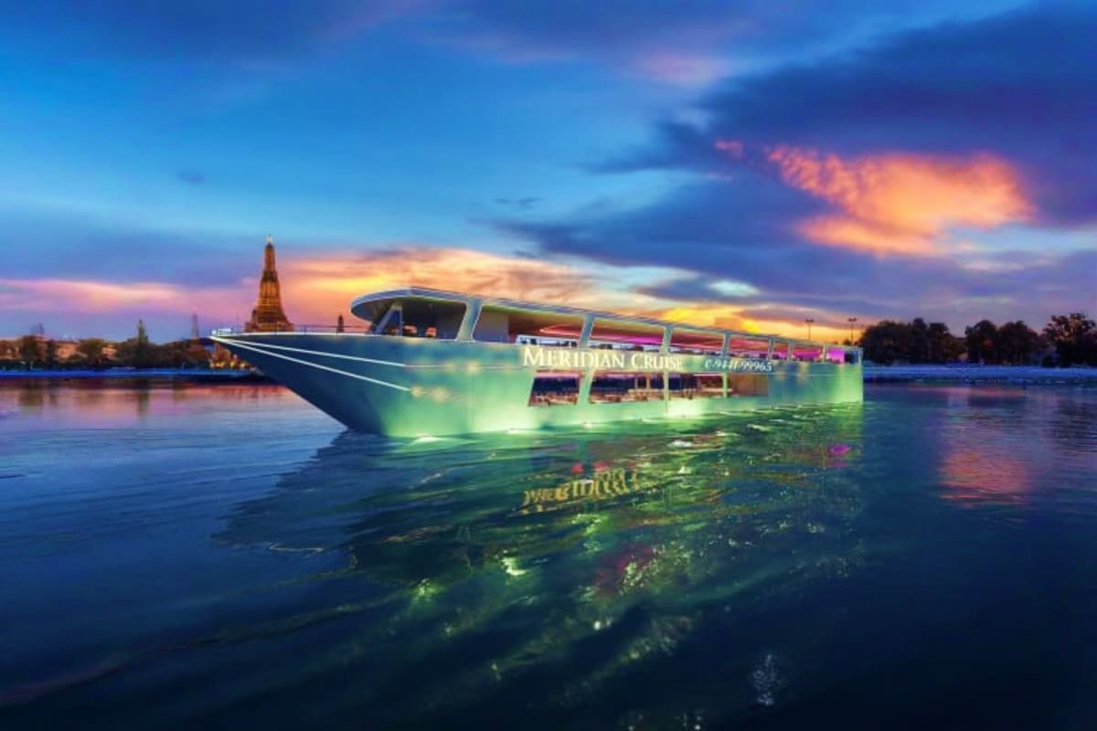 Meridian Cruise boat illuminated at dusk on river with temple spire in background at sunset