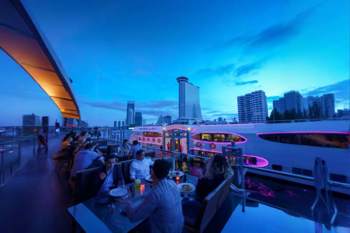 People dining on Grand Pearl Cruise boat deck at dusk with illuminated cityscape and high-rise buildings in background