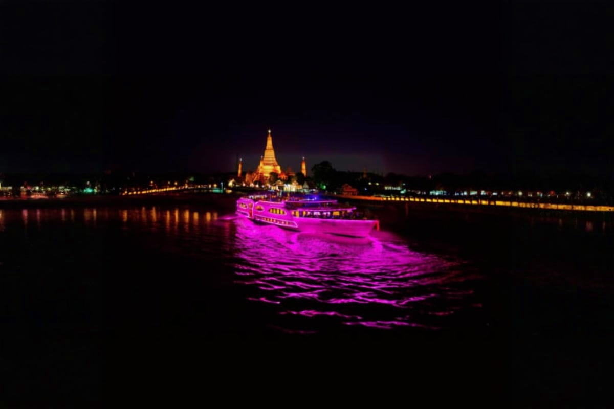 Grand Pearl Cruise Illuminated river cruise boat glowing in magenta on the Irrawaddy River at night with a golden-lit pagoda temple in the backg
