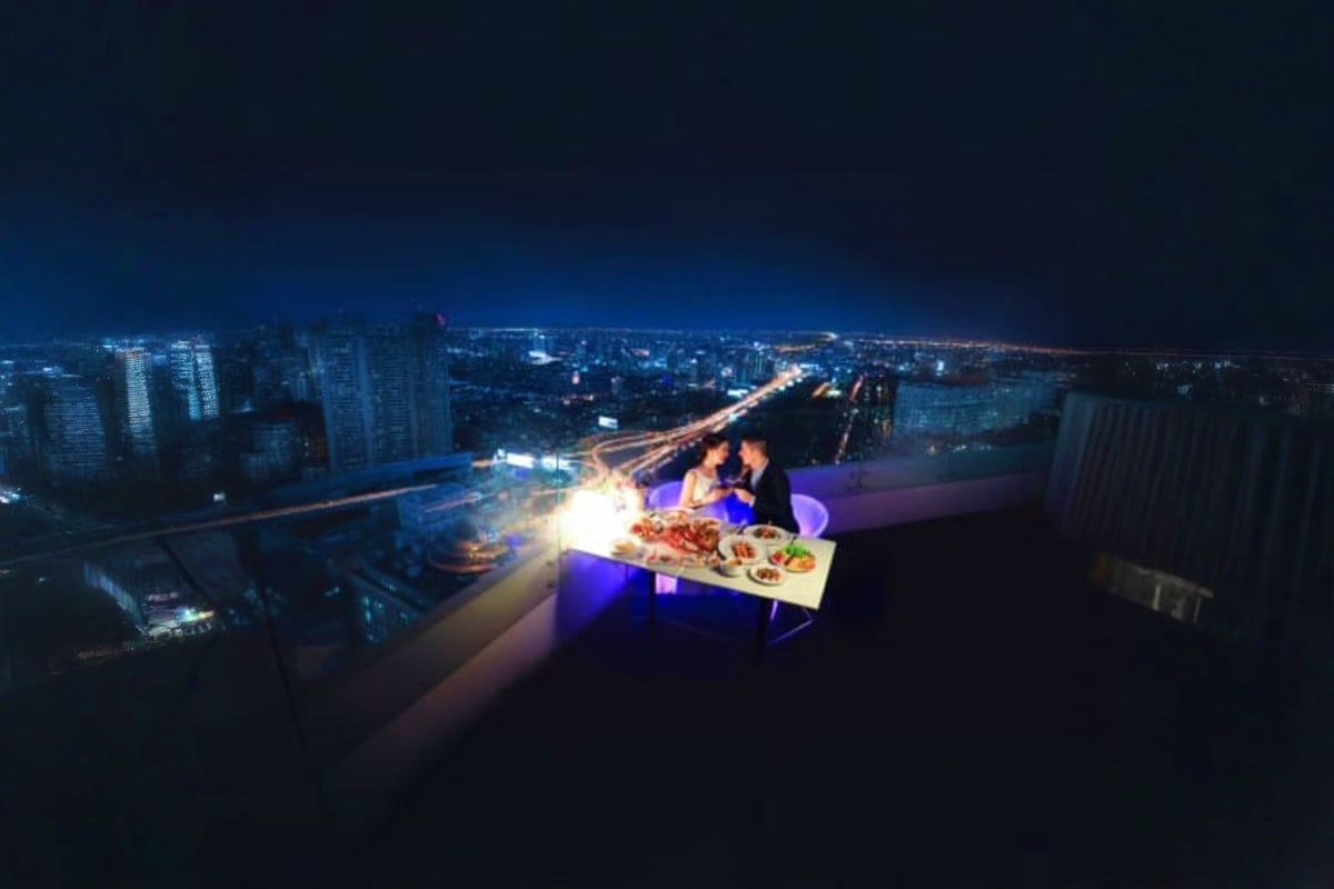Couple dining on rooftop of Baiyoke Sky with illuminated Bangkok cityscape and traffic lights at night