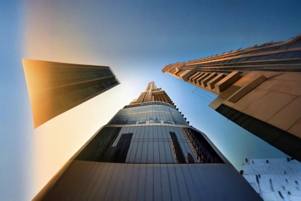 Upward view of Baiyoke Sky skyscraper in Bangkok with surrounding modern buildings against clear blue sky