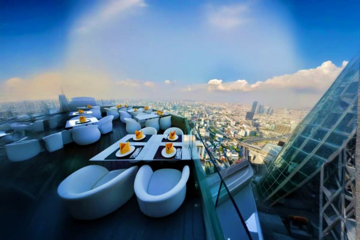 Rooftop dining area at Baiyoke Sky with white pod-shaped seating, tables set with place settings, overlooking sprawling Bangk