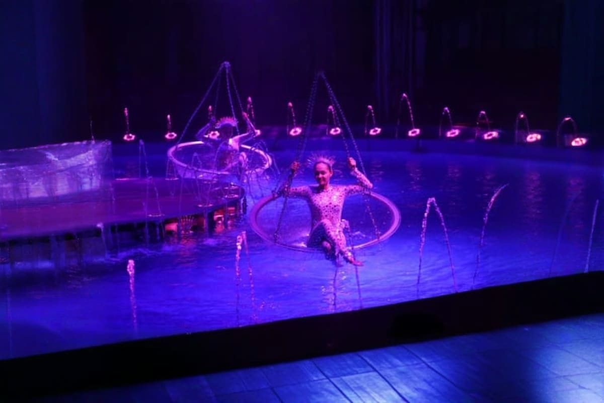 Acrobat performer in sparkly costume inside illuminated hoop during Phuket Aqua Circus stage show with purple lighting and po