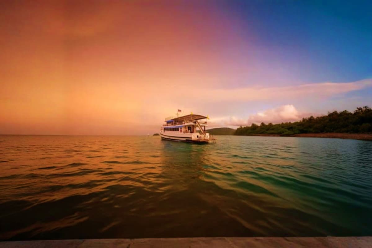 Houseboat anchored in calm waters at sunset with mangrove coastline and colorful sky in background