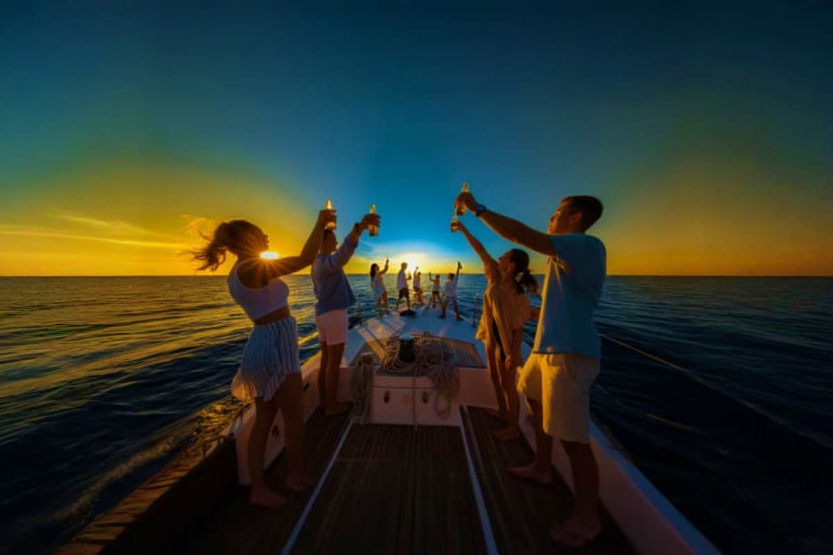 Group of people toasting with drinks on a boat deck during sunset over calm ocean waters