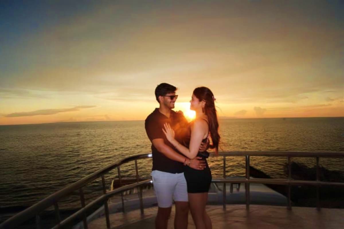 Couple embracing on cruise ship deck at sunset over ocean with sun on horizon