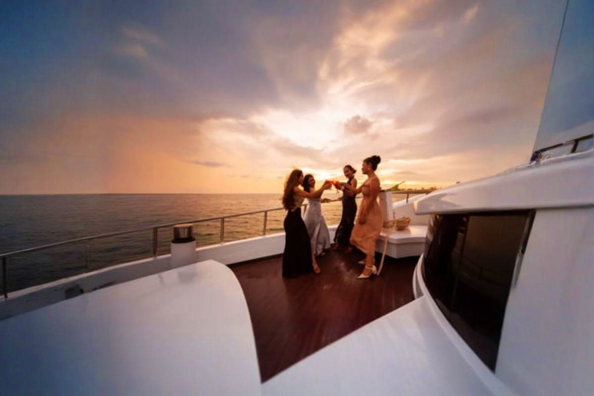 Group of people toasting with drinks on a luxury yacht deck during sunset over calm ocean waters